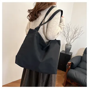 Detail view of a black canvas tote bag worn on shoulder, casual daily style, spacious design.