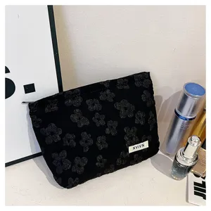 Detailed view of black floral cosmetic pouch with secure zipper on white desktop setup.