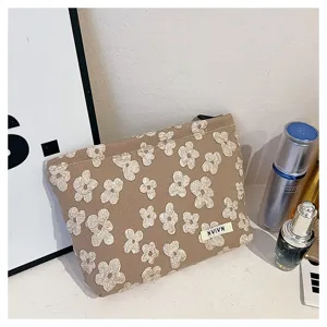 Brown floral cosmetic bag detail shot, featuring embroidered white flowers and a small brand label.