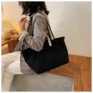Detailed view of casual black canvas tote bag with white straps, worn by model indoors.