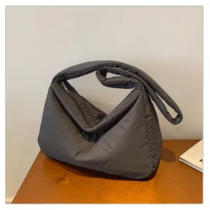 Close-up detail of the dark grey puffer shoulder bag, featuring soft quilted fabric and zipper.