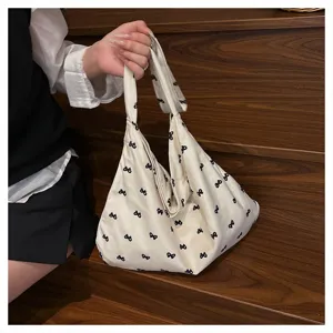 Casual beige canvas shoulder bag with black bow print, stylish slouchy tote bag for women daily use.