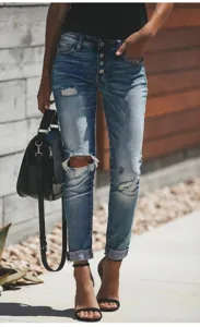 Detail van skinny jeans met blauwe wassing, kapotte knieën en knoopsluiting aan de voorzijde.