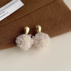 Nahaufnahme flauschiger Kunstpelz Bommel Ohrringe mit goldenem Tropfen Ohrstecker.