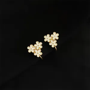Nahaufnahme von vergoldeten, weissen Emaillblumen-Ohrclips mit filigranen Details.