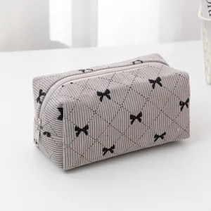 Grey corduroy cosmetic bag detail, featuring black bow embroidery and diamond quilting design.