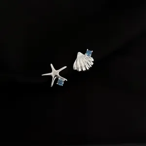 Detailaufnahme asymmetrischer Ohrclips mit Seestern und Muschel sowie blauen Steinen.