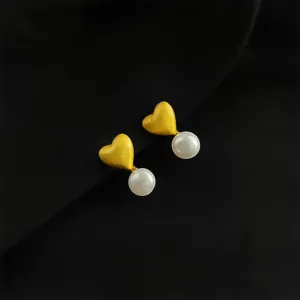 Nahaufnahme von strukturierten Goldherz Ohrringen mit elegantem weißen Perlenakzent.