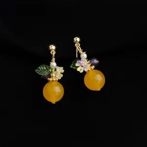Close-up detail of gold-plated clip-on earrings featuring yellow beads and floral leaf charms.