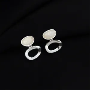Nahaufnahme minimalistischer silberner Ohrclips mit eleganten ovalen weißen Steindetails.