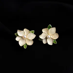 Close-up detail view of elegant white enamel flower earrings with a pearl center and gold trim.