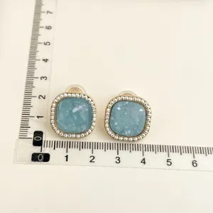 Close-up detail shot of square blue clip-on earrings decorated with white bead borders.