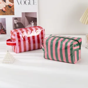 Detail view of colorful striped PVC cosmetic bags on white table, stylish travel wash pouch.