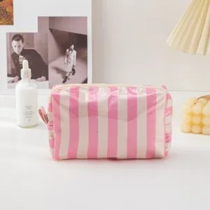 Detailed shot of pink and white striped PVC cosmetic bag on white surface with lifestyle props.
