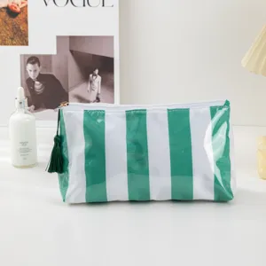 Close-up detail view of the green and white striped PVC cosmetic bag with a cute tassel zipper pull.