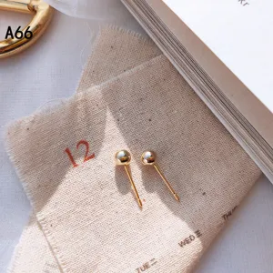 Detailaufnahme von minimalistischen Goldkugel-Ohrringen auf strukturiertem Leinenstoff.