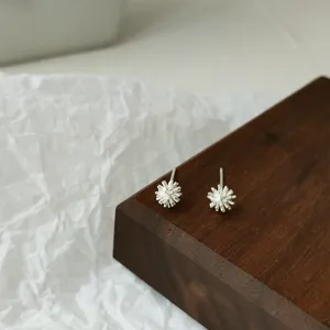 Detaillierte Nahaufnahme minimalistischer silberner Ohrstecker auf einem stilvollen Holzblock.