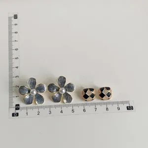 Detailed shot of stylish grey flower pearl earrings and black gold checkered crystal stud earrings.