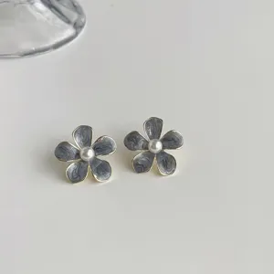 Close-up of grey floral oil-drop earrings with pearl center and sleek gold-tone rim detail.