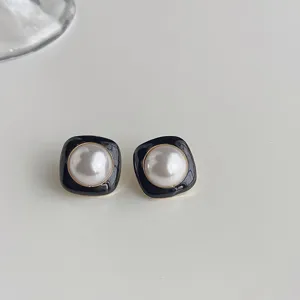 Detail shot of black enamel square pearl earrings with gold trim, elegant fashion jewelry accessory.