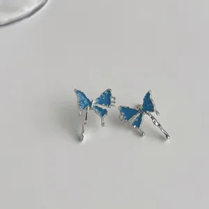 Close-up of blue dripping butterfly silver stud earrings, delicate minimalist detail jewelry.
