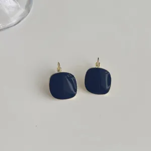 Close-up detail of stylish dark blue enamel square drop earrings with elegant gold trim.