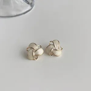 Close-up detail of elegant white and gold abstract knotted stud earrings on clean background.