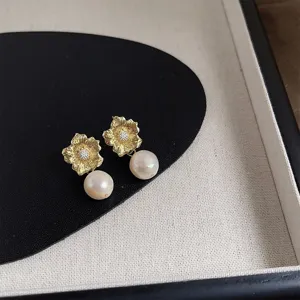 Detailaufnahme von eleganten goldenen Blumen-Ohrsteckern mit hängenden Süßwasserperlen.