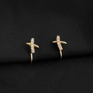Detailansicht vergoldeter Kreuz-Ohrclips mit funkelnden Zirkoniasteinen auf schwarzem Stoff.
