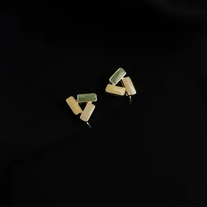 Detailed view of geometric clip-on earrings with green and beige enamel blocks on black.