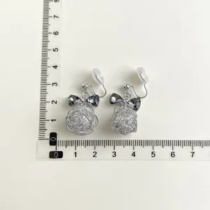 Detail shot of clip-on earrings featuring wire-wrapped ball and crystal bow elements.
