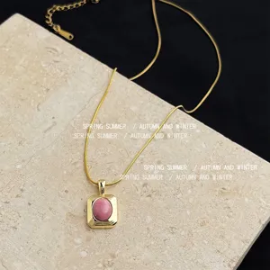 Gold stainless steel necklace with square pendant and pink stone detail close up view.