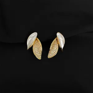 Nahaufnahme goldener Ohrringe mit Zirkonia und weißem Emaille auf schwarzem Stoff.