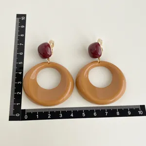 Elegante Ohrclips mit großen karamellfarbenen Kreolen und dunkelroten Tops mit Maßstab.