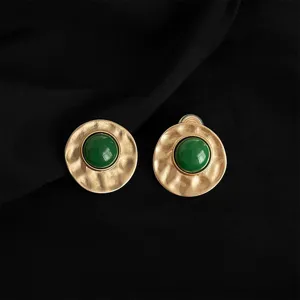 Nahaufnahme Detail von vintage Stil gold texturierte runde Clip-Ohrringe mit gruenem Schmuckstein.