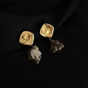Nahaufnahme von goldenen, unregelmäßigen Clip-Ohrringen mit dunklen Rohkristall-Anhängern.