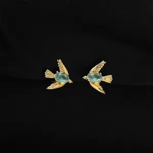 Detailaufnahme vergoldeter Schwalben-Ohrclips mit blauen Steinen, schmerzfreies Design.
