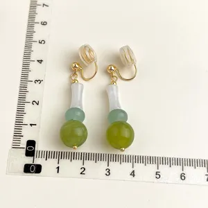 Eleganti orecchini a clip con pendenti di perle verdi sfumate e dettagli di colore dorato.