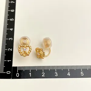 Nahaufnahme von vergoldeten Ohrclips mit glitzerndem Zirkon und praktischem Messlineal.
