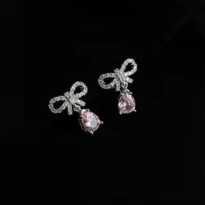 Detailed close-up shot of sparkling rhinestone bow earrings with delicate pink pear-cut drop stones.