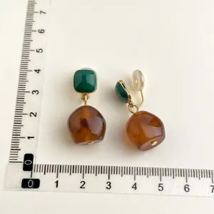 Orecchini a clip senza foro con quadrato verde e ciondolo ambrato, con righello di misurazione.