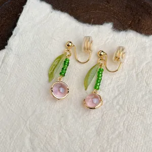 Dettaglio in primo piano di orecchini a clip con gemma rosa, foglia verde e perle.
