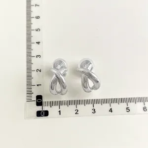 Detailed view of silver-colored twisted ribbon clip-on earrings displayed with measuring ruler.