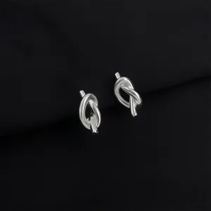 Close-up detail shot of elegant silver knot earrings on black background, premium jewelry texture.