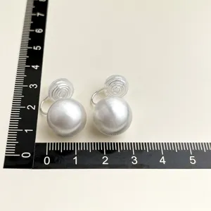 Nahaufnahme von Clip-On-Perlenohrringen mit Lineal zur genauen Grössenmessung und Details.