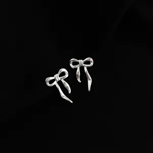 Silver bow earrings detail view, minimalist metal jewelry design showcasing fine craftsmanship.