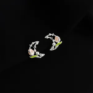 Detailed shot of silver-tone crescent moon tulip pearl earrings with enamel and rhinestones.