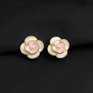 Nahaufnahme von eleganten doppelten Kamelien-Ohrringen mit Goldrand und Perlendetail.