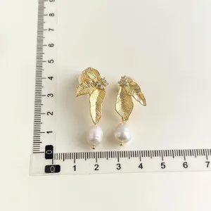 Nahaufnahme der vergoldeten Blatt Ohrringe mit Zirkoniasteinen und feinen Perlen im Detail.