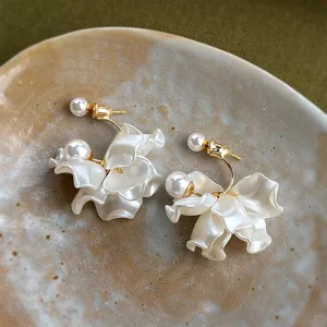 Close-up detail of handmade flower earrings with pearls and gold accents on a ceramic plate.